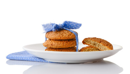 Stack of three homemade oatmeal cookies tied with blue ribbon in small white polka dots and halves of cookies on white ceramic plate on matching blue napkin, isolated on white background