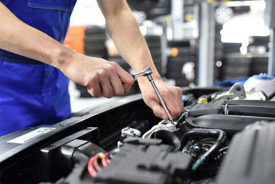 Automechaniker repariert an einem Fahrzeug im Motorraum - closeup // mechanic repairs engine of a car