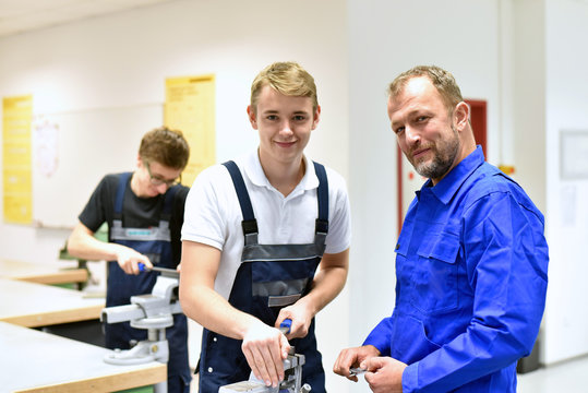 Berufsausbildung in der Metallbranche - Meister und Lehrling am Schraubstock l&auml;cheln // Smiling instructor and trainee