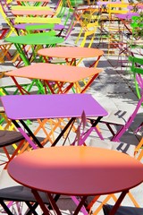 Des tables rondes et carrées de toutes les couleurs sur une terrasse en extérieur