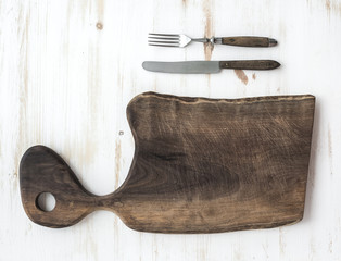 Kitchen-ware set. Old rustic chopping board made of walnut wood, knife, fork on a white background