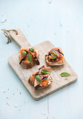 Bruschettas with Prosciutto, roasted melon, soft cheese and basil on wooden serving board over light blue background