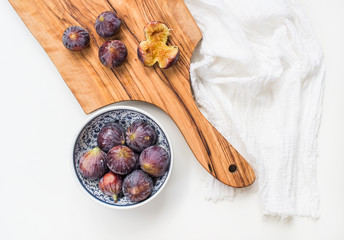 Fresh figs in blue patterned ceramic bowl and on olive wood board over white background