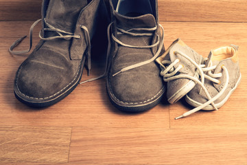 Closeup of father's shoes close to child's shoes on a parquet