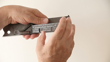 A man makes adjustments to blocks of metal type in his composing stick tool.