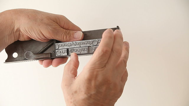 A man makes adjustments to blocks of metal type in his composing stick tool.