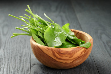 fresh sorrel leaves in olive bowl on oak wood table