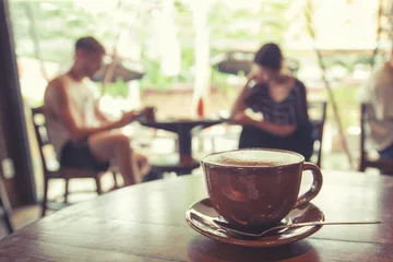 Selbstklebende Fototapeten Cup of coffee on table in cafe with people retro instagram effect - shallow depth of field © jakkapan