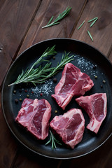 Frying pan with raw lamb T-bone steaks and seasonings, top view