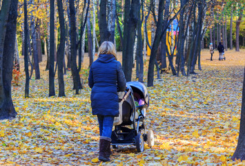 Mother with stroller walking on a rainy day in autumn park