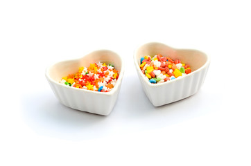 Fototapeta na wymiar Colorful Heart Cake Sprinkles for cake decoration in white ceramic heart shape Cup isolated in white background