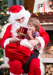 Happy child with gift sitting on Santa Claus lap