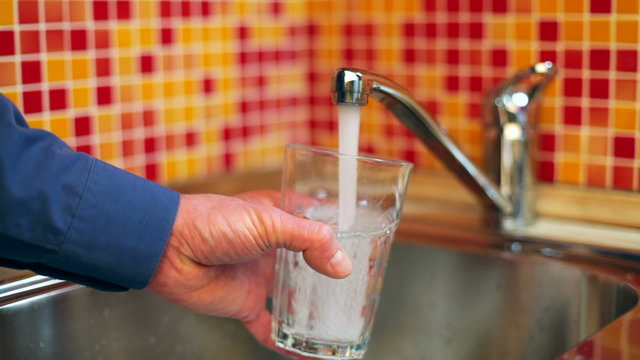Man pouring a glass of fresh water from a kitchen faucet