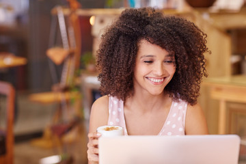 Mixed race woman with afro hair using her laptop in a coffee sho