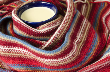 Cup of cocoa/coffee with milk. Knitted striped texture. Scarf.