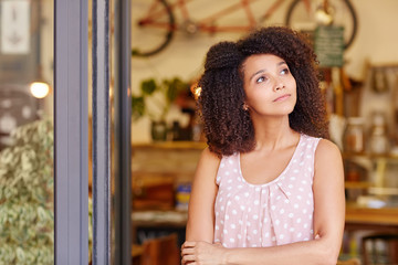 Small business owner standing and thinking in the door of her co
