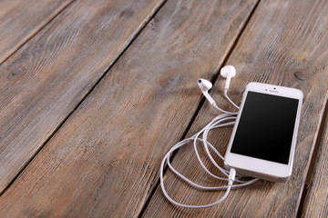 White cellphone with headphones on wooden background