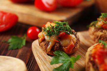 A wooden tablet with stuffed mushrooms and vegetables on the table, close-up