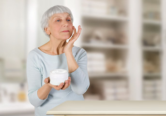 charming elderly woman applying cosmetic cream on her face for facial skin care in bathroom