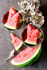 Sliced watermelon in metal bowl with flowers on grey background, close up