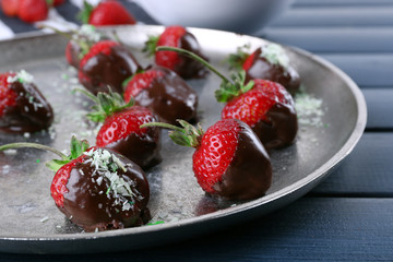 A plate of strawberries in chocolate on blue wooden background