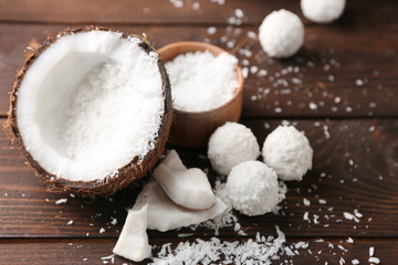 Candies in coconut flakes, glass of milk and fresh coconut on dark wooden background