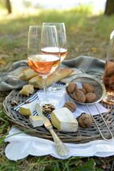 Picnic theme - rose wine, cheese, baguette and nuts on wicker tray, outdoors