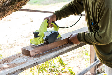 worker planing a plank of wood with a electric plane