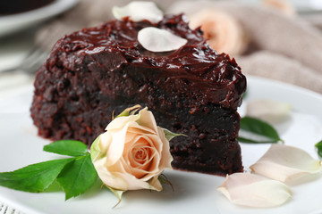 Piece of chocolate cake decorated with flowers on white wooden table