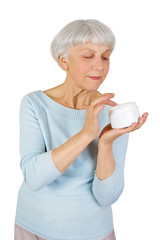charming elderly woman applying cosmetic cream on her face for facial skin care on a white background