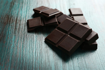 Black chocolate pieces on color wooden background