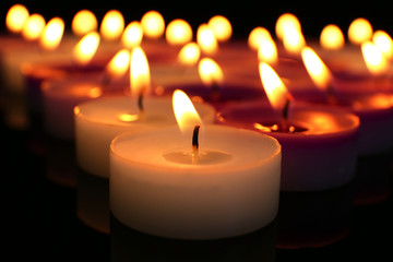 Many burning small candles on dark background, close-up