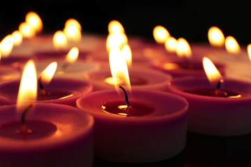 Many burning small candles on dark background, close-up