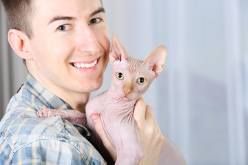 Young handsome man holding a cat on light background