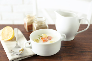 Delicious salmon cream soup on wooden table, which served with sliced lemon and spices