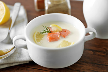 Delicious salmon cream soup on wooden table, which served with sliced lemon and spices