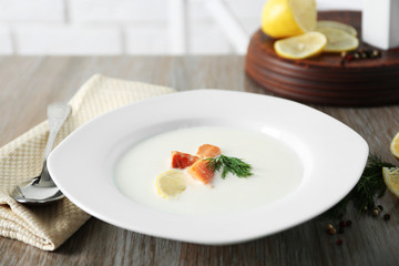 Delicious cream soup with fish and sliced lemon on white table in the restaurant