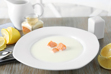 Delicious salmon cream soup in white plate on wooden table, close up