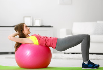 Fototapeta na wymiar Beautiful young girl doing exercises with fit ball at home