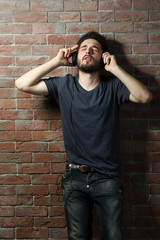 Young handsome man listening music with headphones on brick wall background