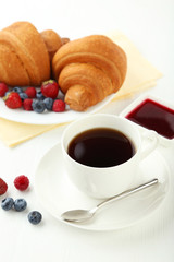 Fresh tasty croissants with berries and coffee on white wooden b