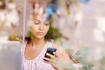 Woman using her phone seen through the window of a coffee shop