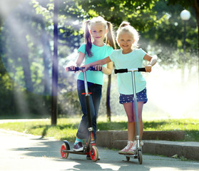 Fototapeta premium Small girls riding on scooters in park