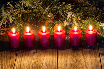 Glowing red candles with snow covered evergreen branch on rustic