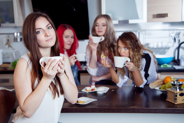 friends drink tea and coffee at kitchen, portrait of  young beautiful brunette in the foreground, woman with white cup