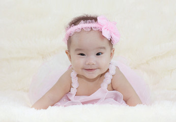Cute baby girl on a soft white carpet. In a beautiful pink dress