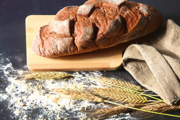 rustic crusty bread and wheat ears on a dark wooden table