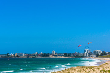 Obraz premium Ocean beach with kite surfers and city skyline in a distance
