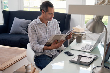 Smiling man reading business magazine at home office desk