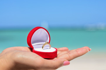 Female hand holding golden wedding ring in red jewellery box on